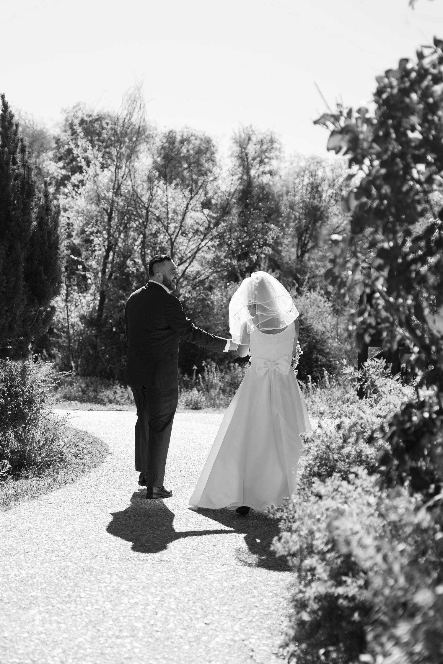 Black and white photo of a couple walking together on a garden path during their wedding.
