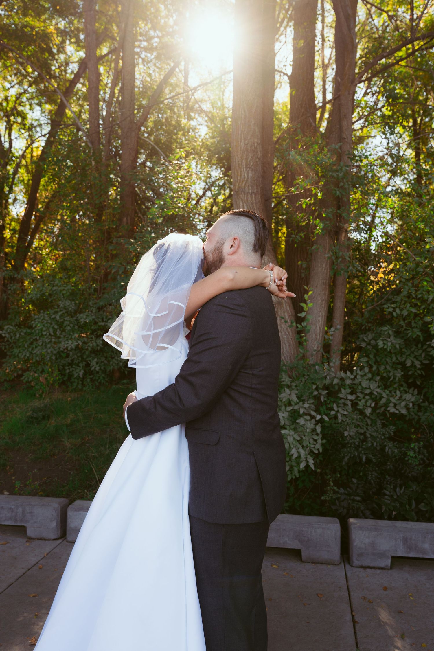 Golden sunlight illuminates a tender embrace between newlyweds surrounded by autumn trees.