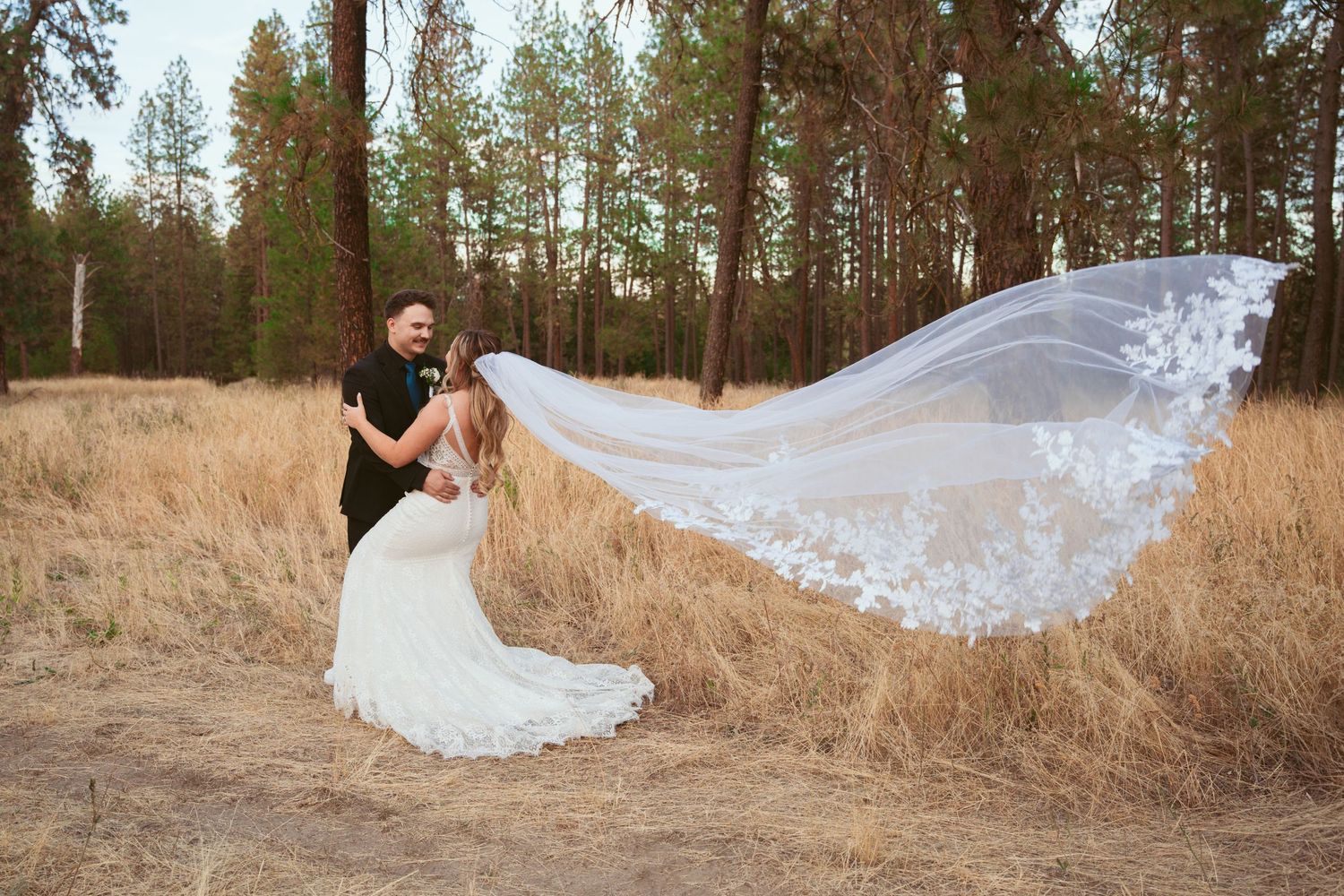Dramatic flowing veil shot in a rustic forest setting with pine trees in background.