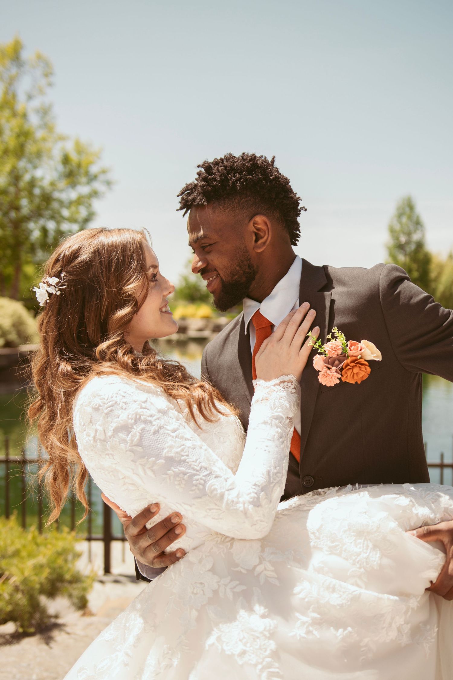 A joyful wedding couple embracing outdoors in elegant attire with floral accents.
