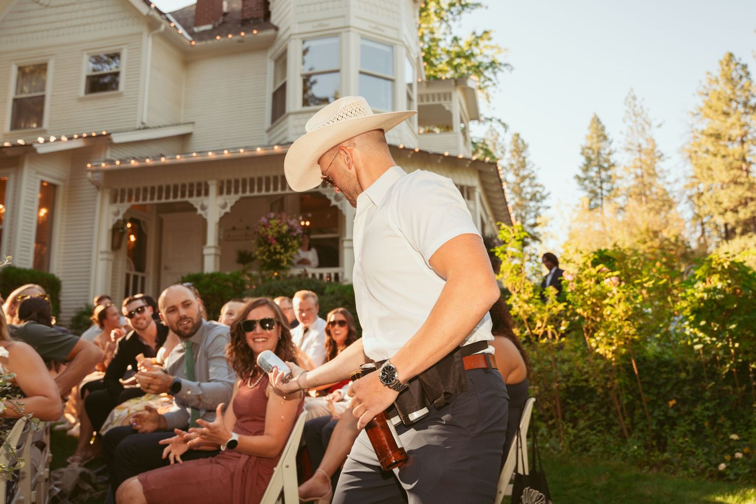 Outdoor wedding reception at a charming white Victorian-style house in late afternoon light.