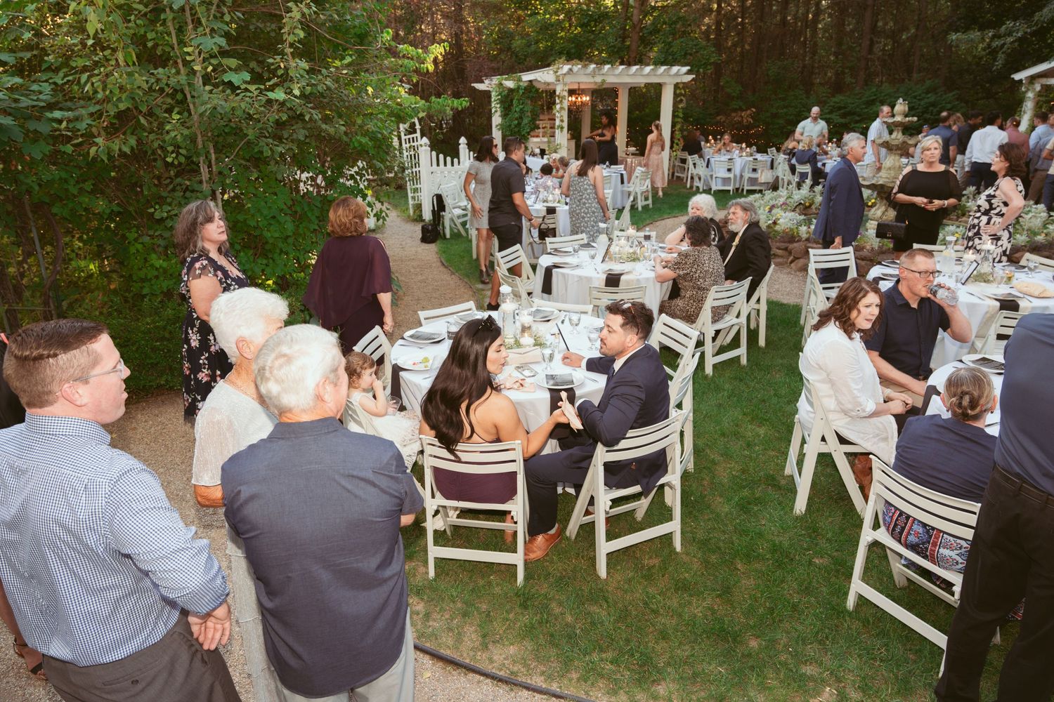 Outdoor wedding reception setup with white chairs arranged on a garden lawn.