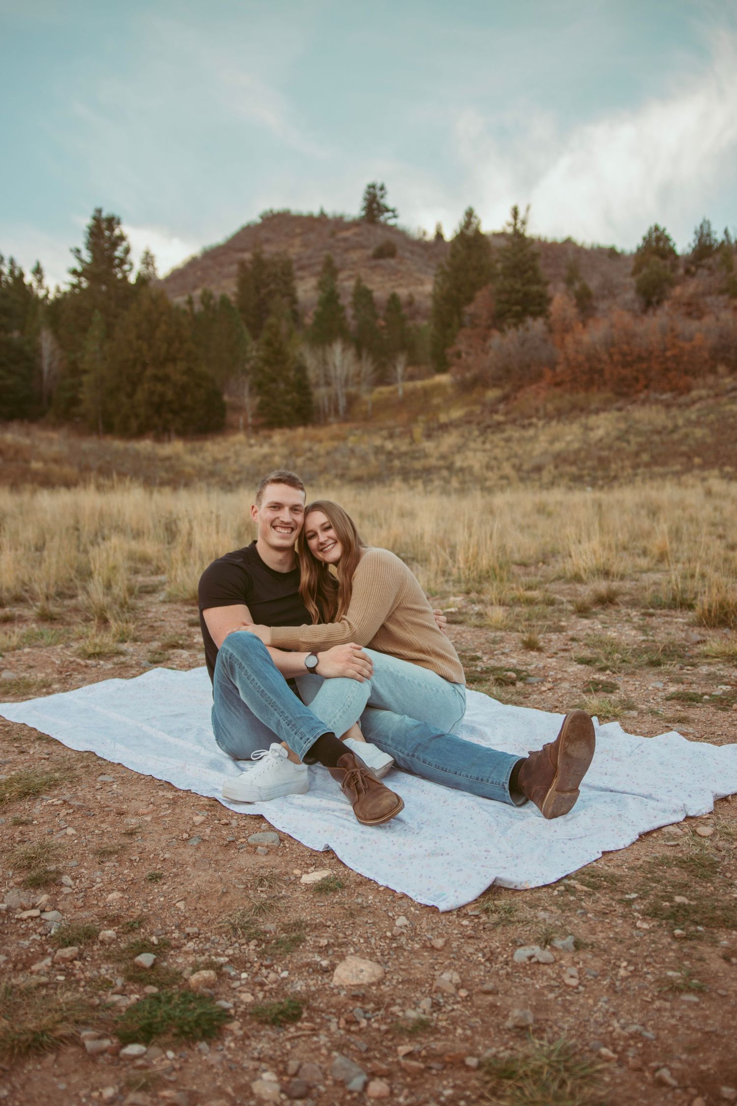 Couple sharing tender moment while resting on blanket in mountainous terrain.
