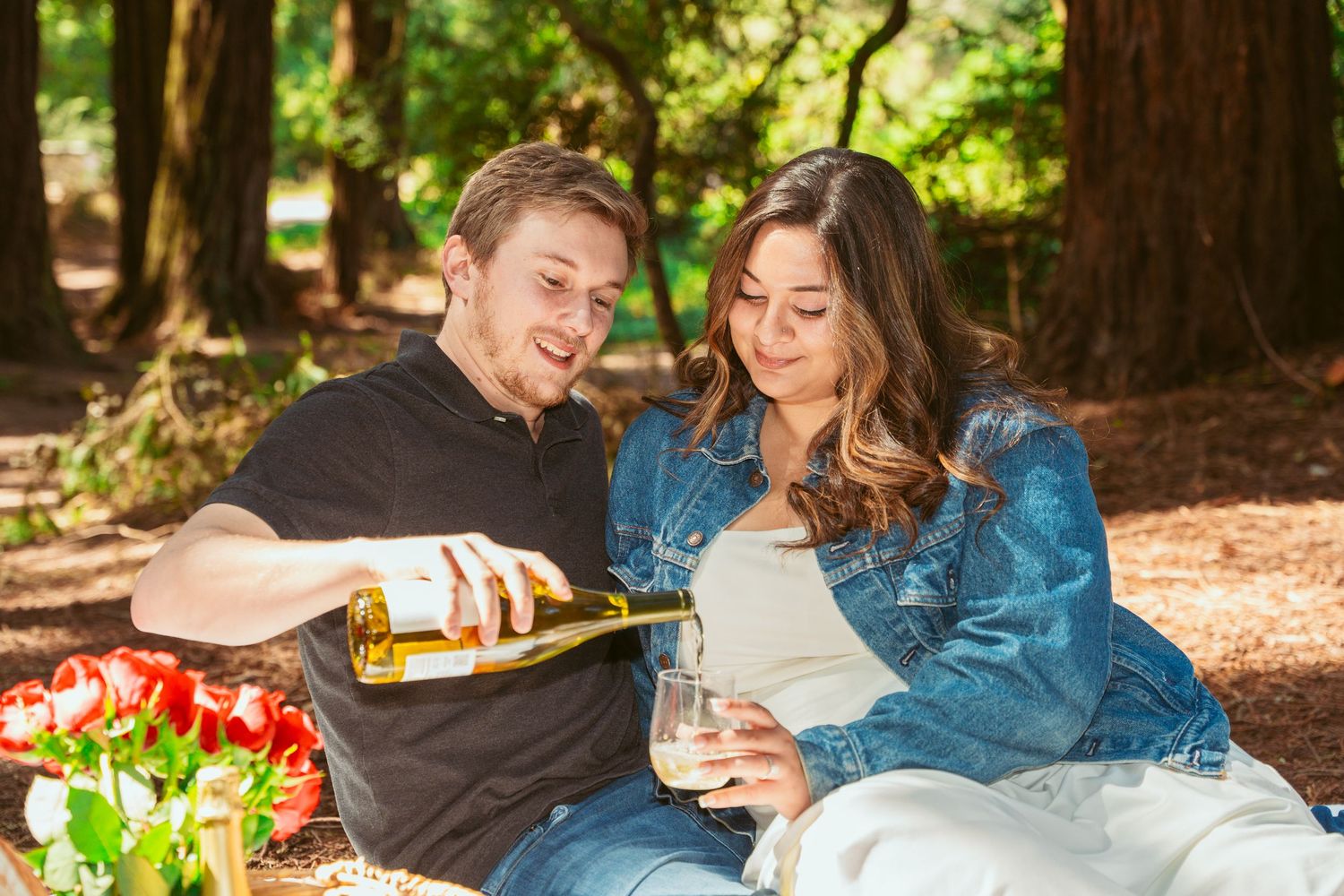 Romantic couple enjoying drinks and laughter in a sunlit forest setting.