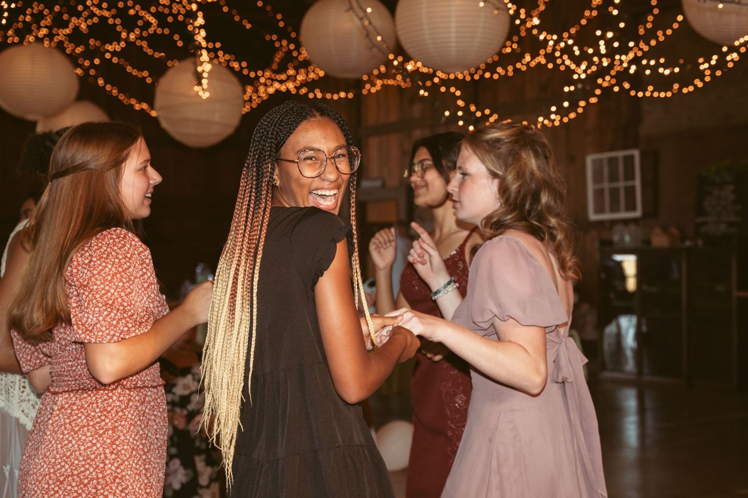 Friends dancing together at a celebration under twinkling lights and paper lanterns.