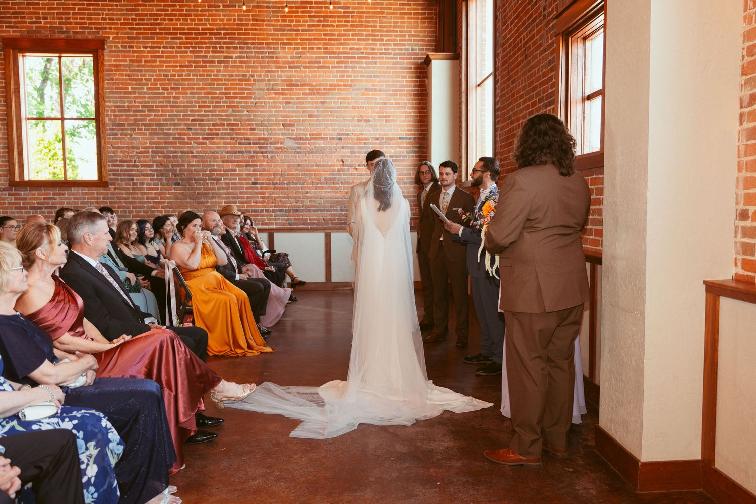 Wide panoramic view of wedding ceremony in industrial brick venue with natural lighting.