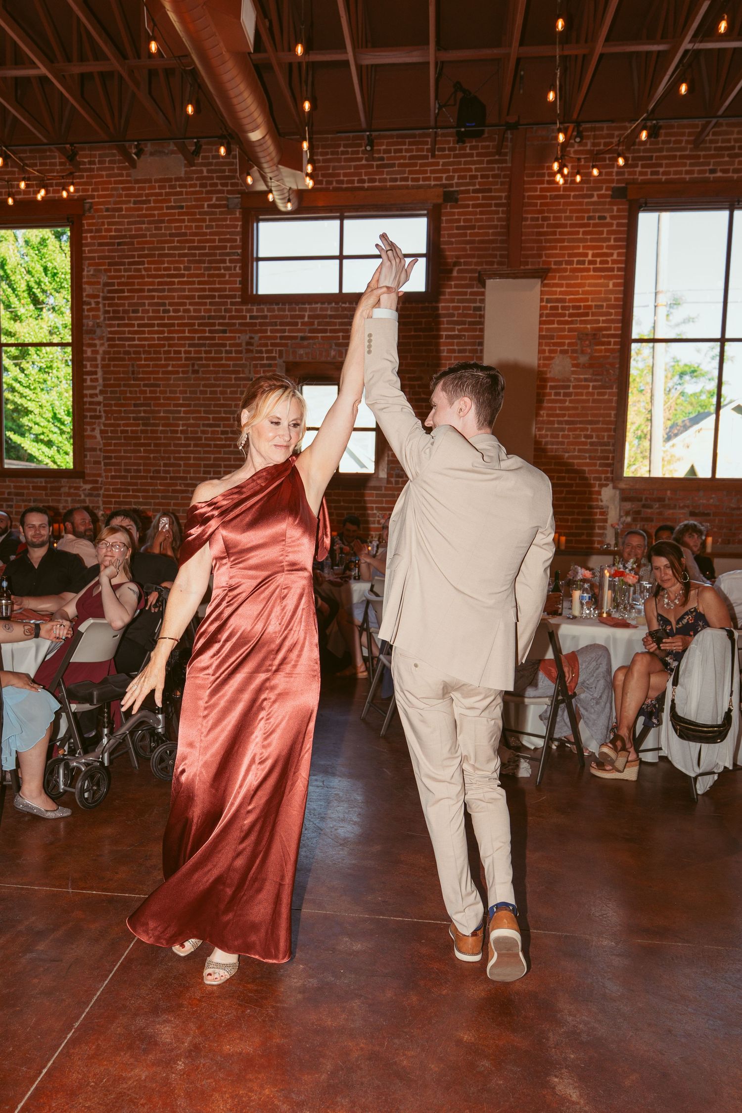 Wedding dancers performing enthusiastic moves on a dark wooden floor in a brick venue.