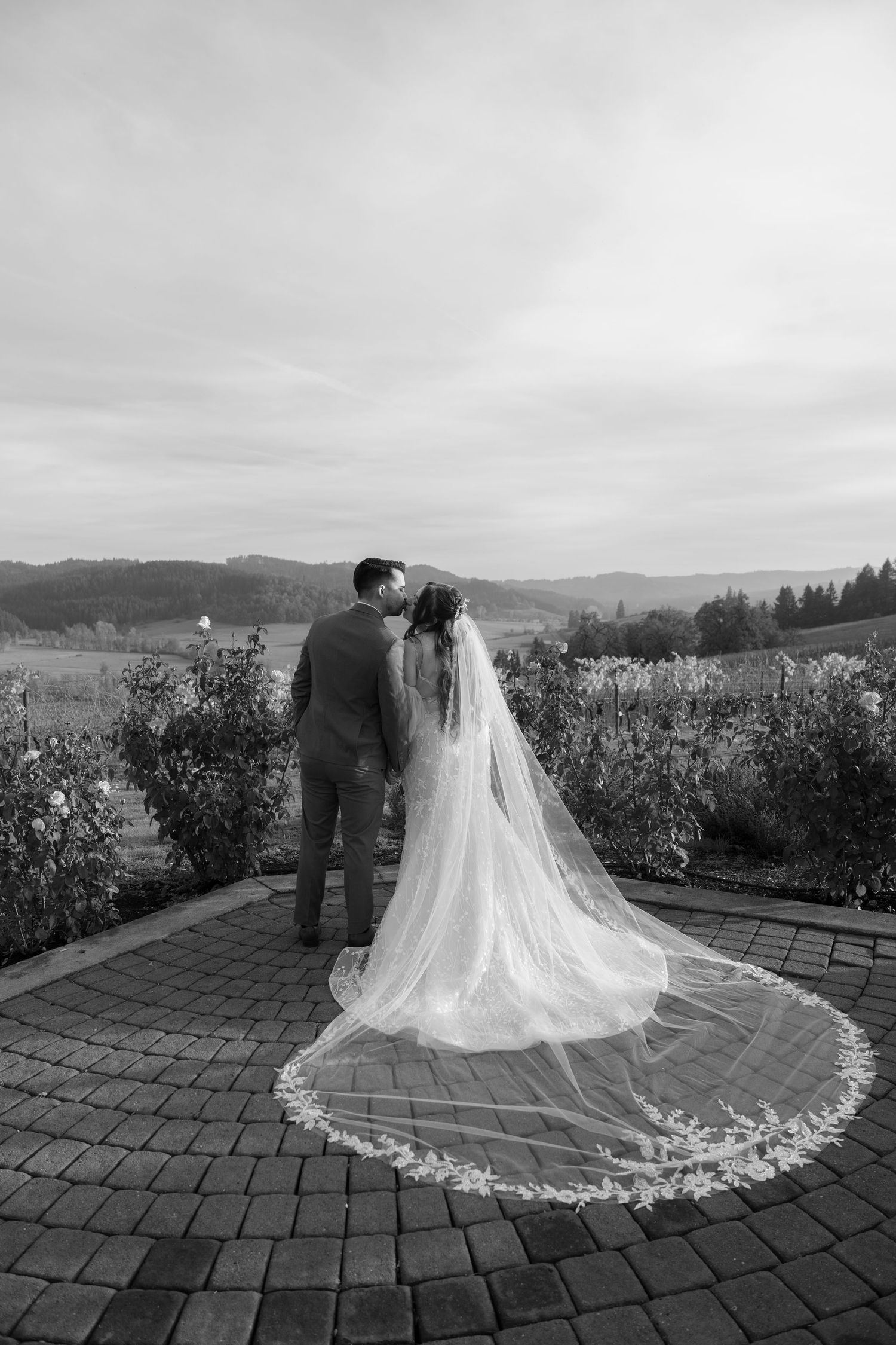 Black and white wedding photo showing couple on brick patio with dramatic cathedral veil.