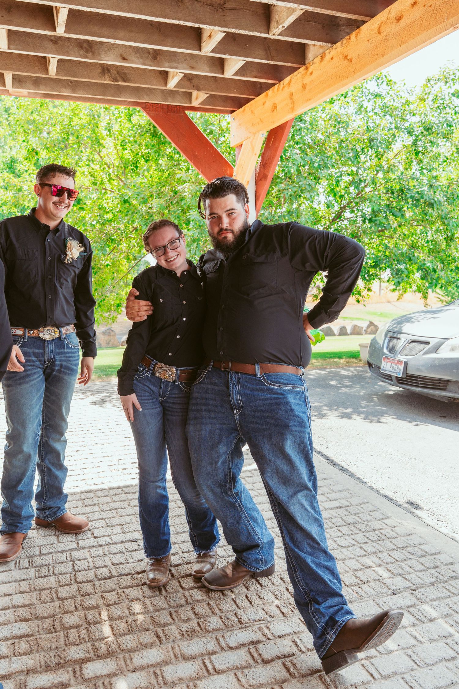 Groomsmen in black shirts and jeans perform synchronized jumping poses under wooden pavilion.
