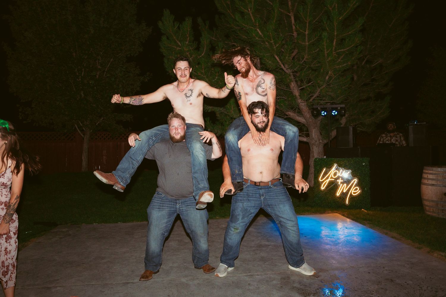 Wedding party members performing energetic dance moves at an outdoor reception.