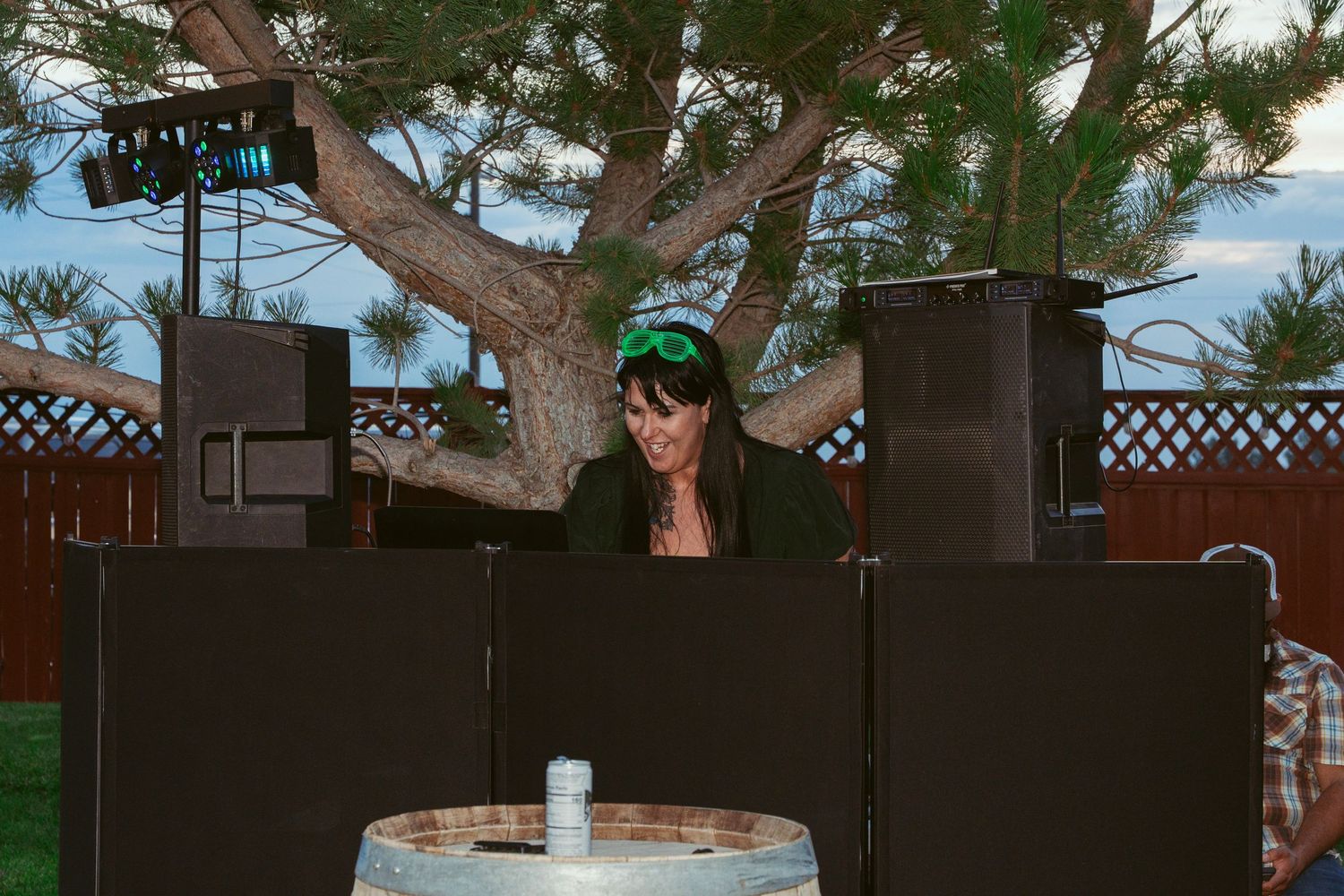 DJ booth setup against wooden fence at outdoor wedding reception.