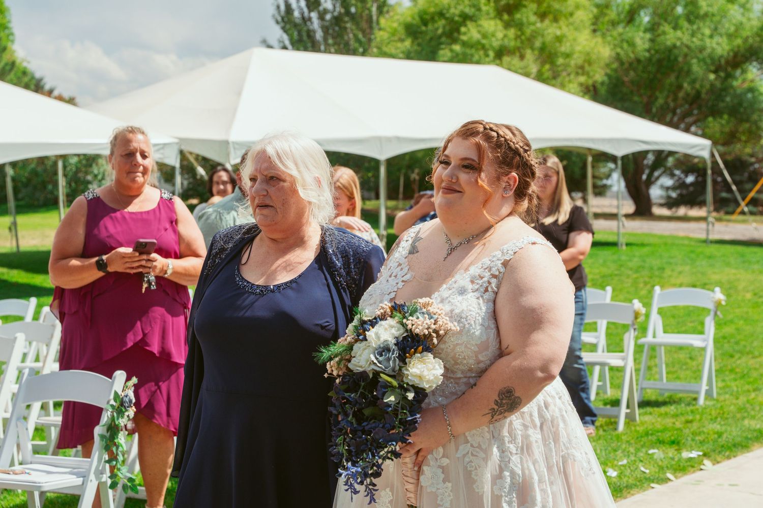 Outdoor wedding ceremony setup with white chairs on a lush green lawn surrounded by trees.