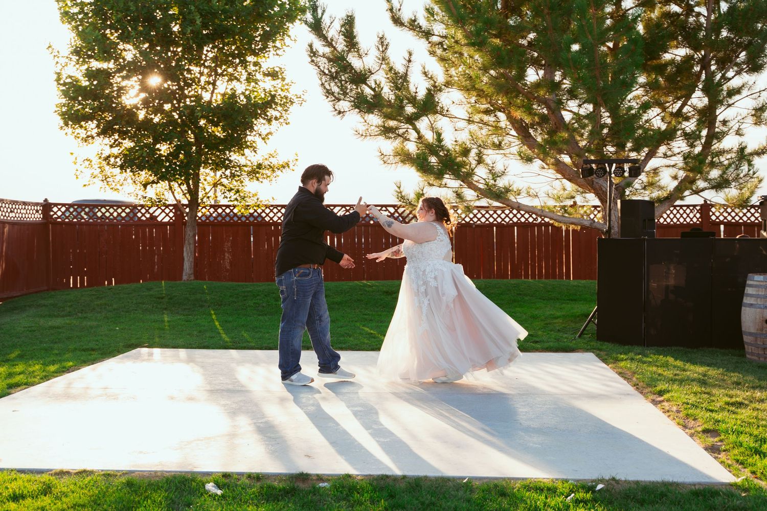 People dancing in a line formation at an outdoor wedding reception with trees in the background.