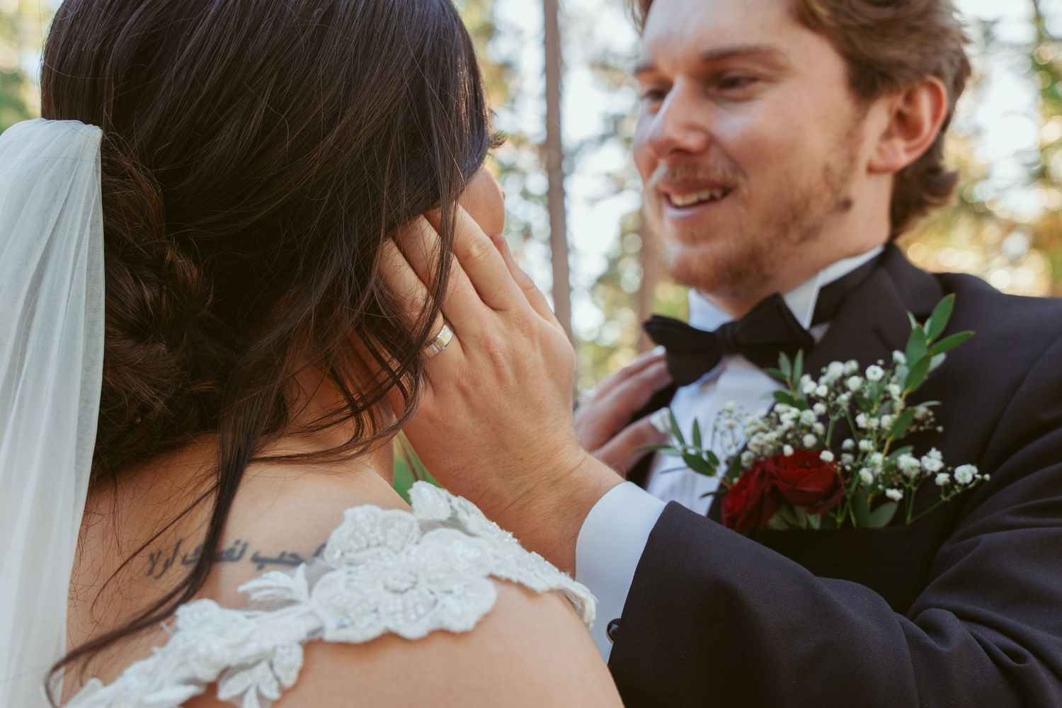 A candid moment between newlyweds sharing an intimate moment outdoors with the groom holding a boutonniere.