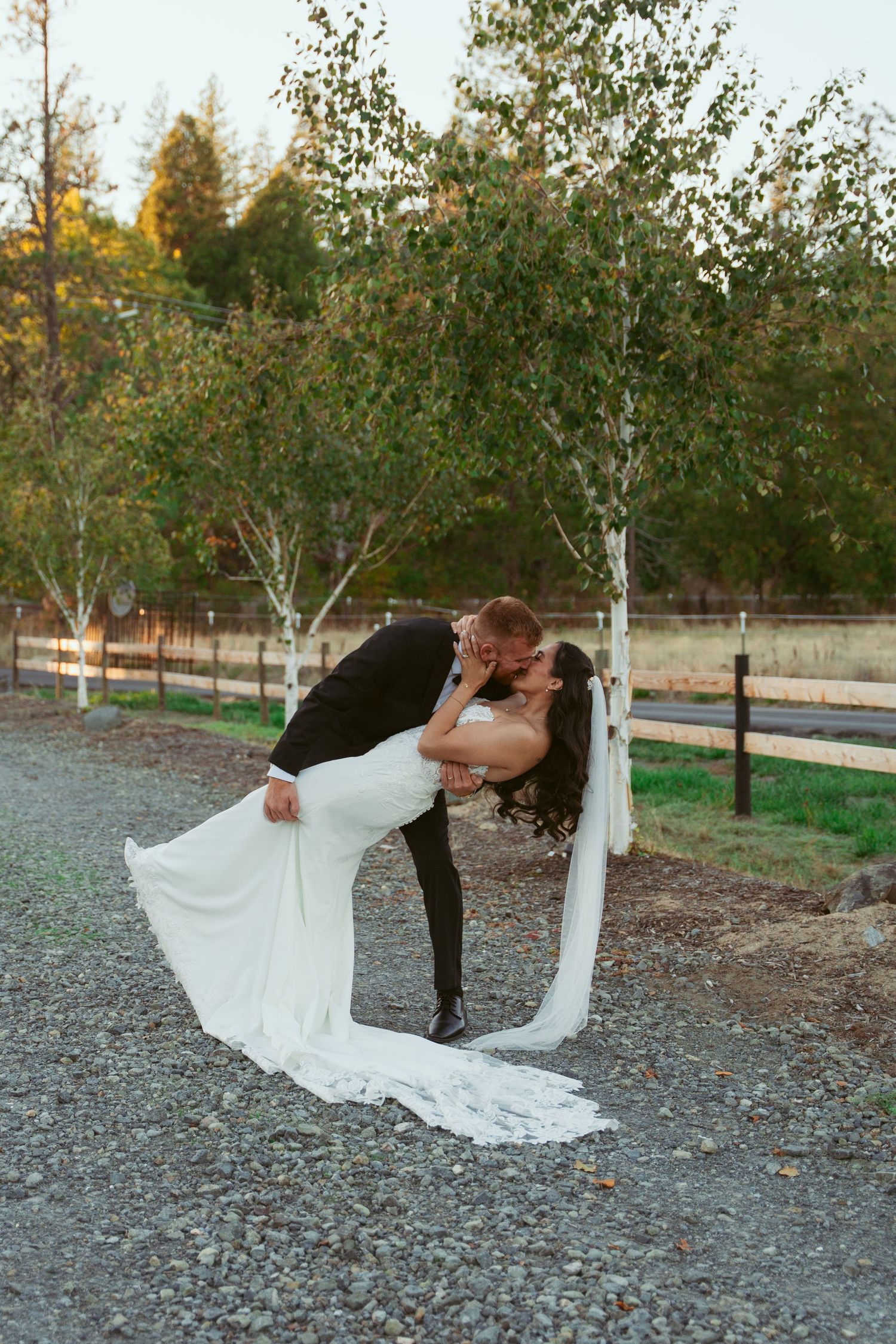 Romantic dip kiss on a gravel path with bride's veil flowing dramatically.