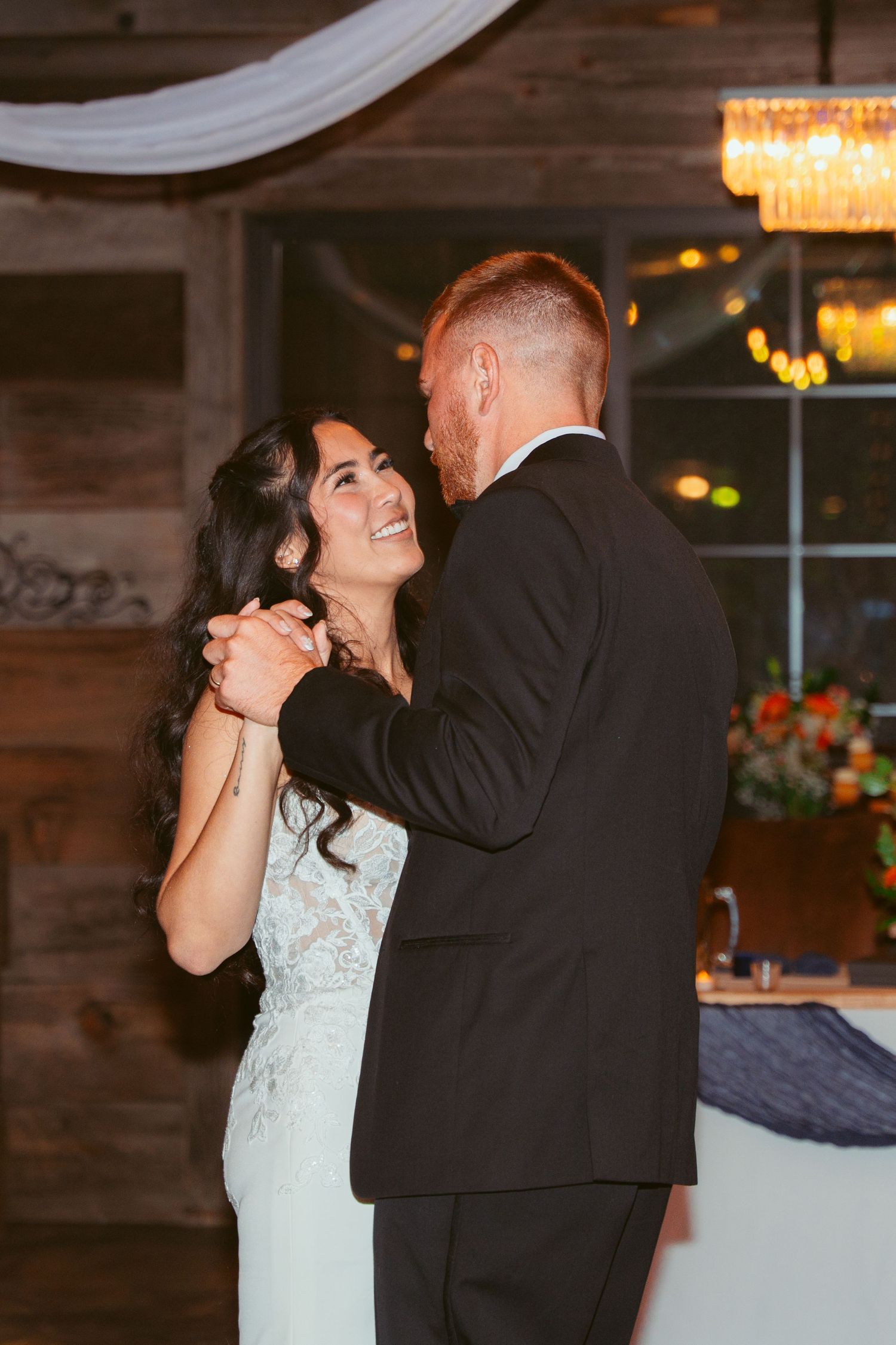 Newlyweds share an intimate dance moment in a rustic venue with mood lighting.