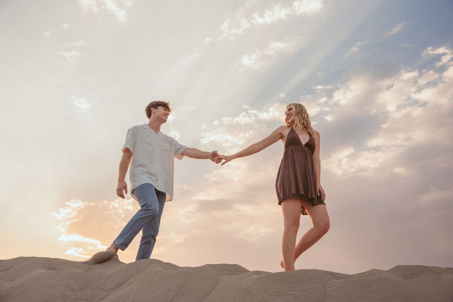 Romantic couple poses playfully in a desert landscape at sunset with sand dunes in the background.