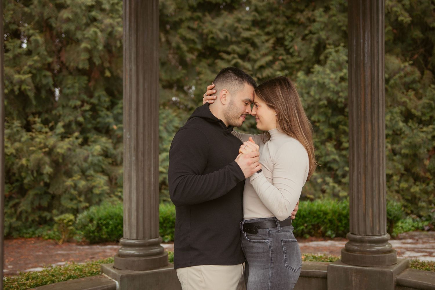 Romantic couple embracing in front of rustic wooden pillars in a garden setting.