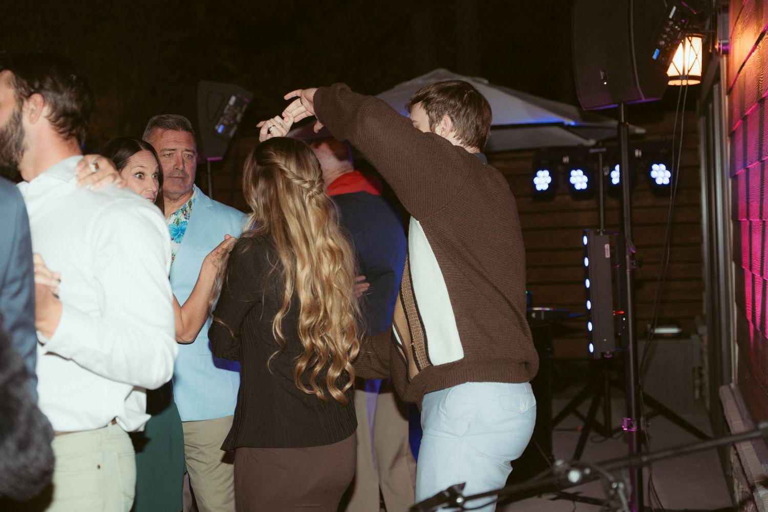 People dancing energetically at a nighttime outdoor party with stage lighting.
