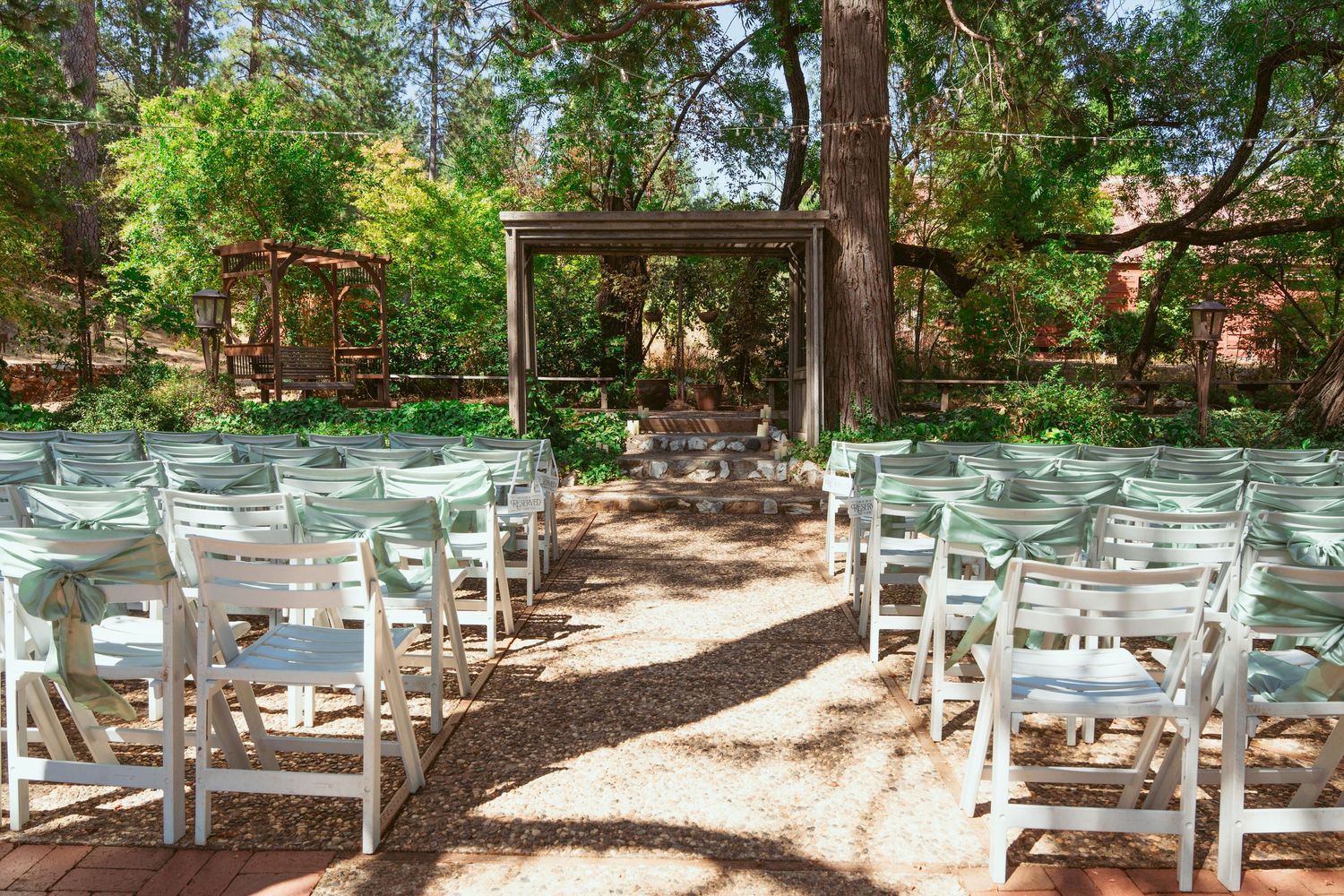 White folding chairs arranged in rows under shady trees for an outdoor ceremony.