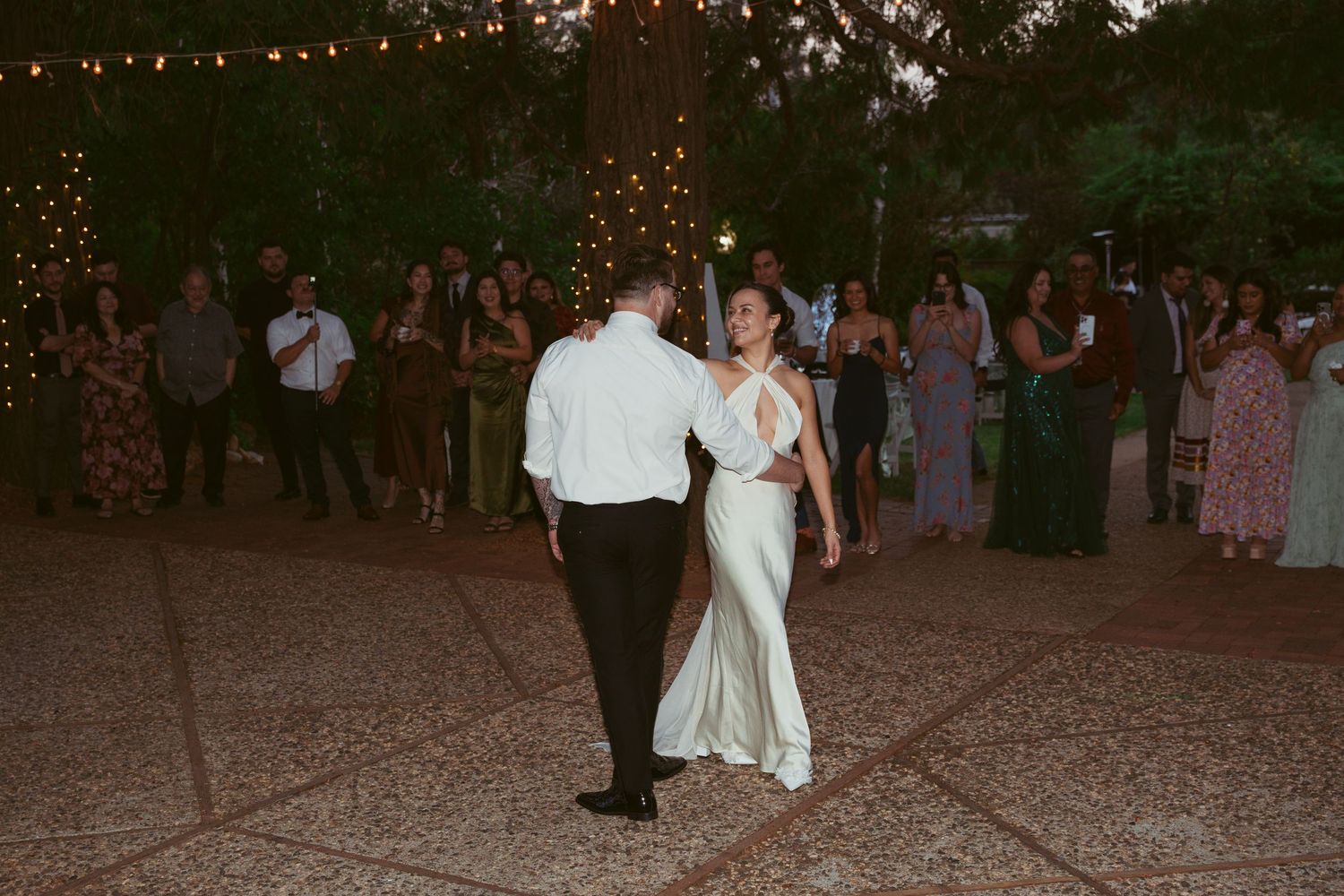 A couple shares a romantic dance at their evening wedding reception under string lights.
