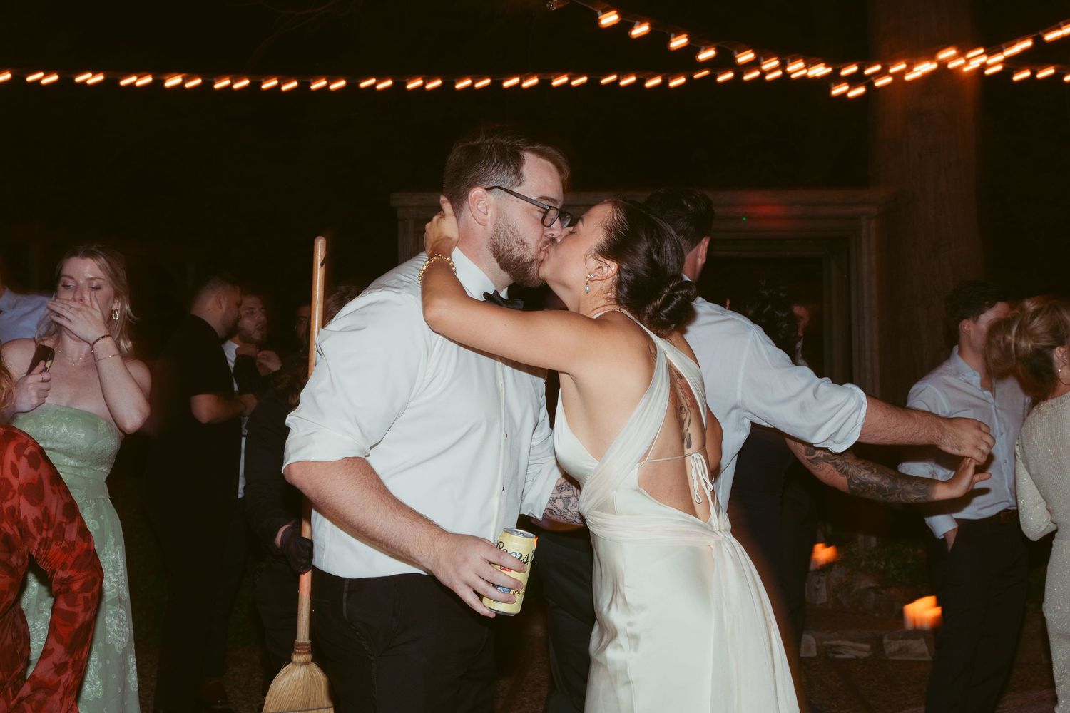 Wedding reception guests dancing and celebrating under warm string lights at an evening party.
