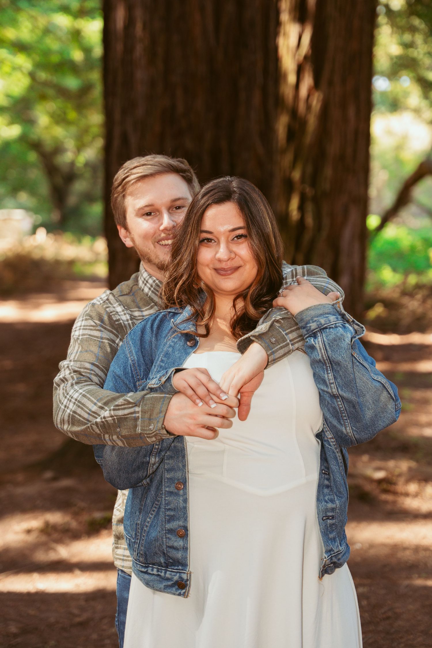 Couple shares an affectionate moment in a sun-dappled redwood forest.