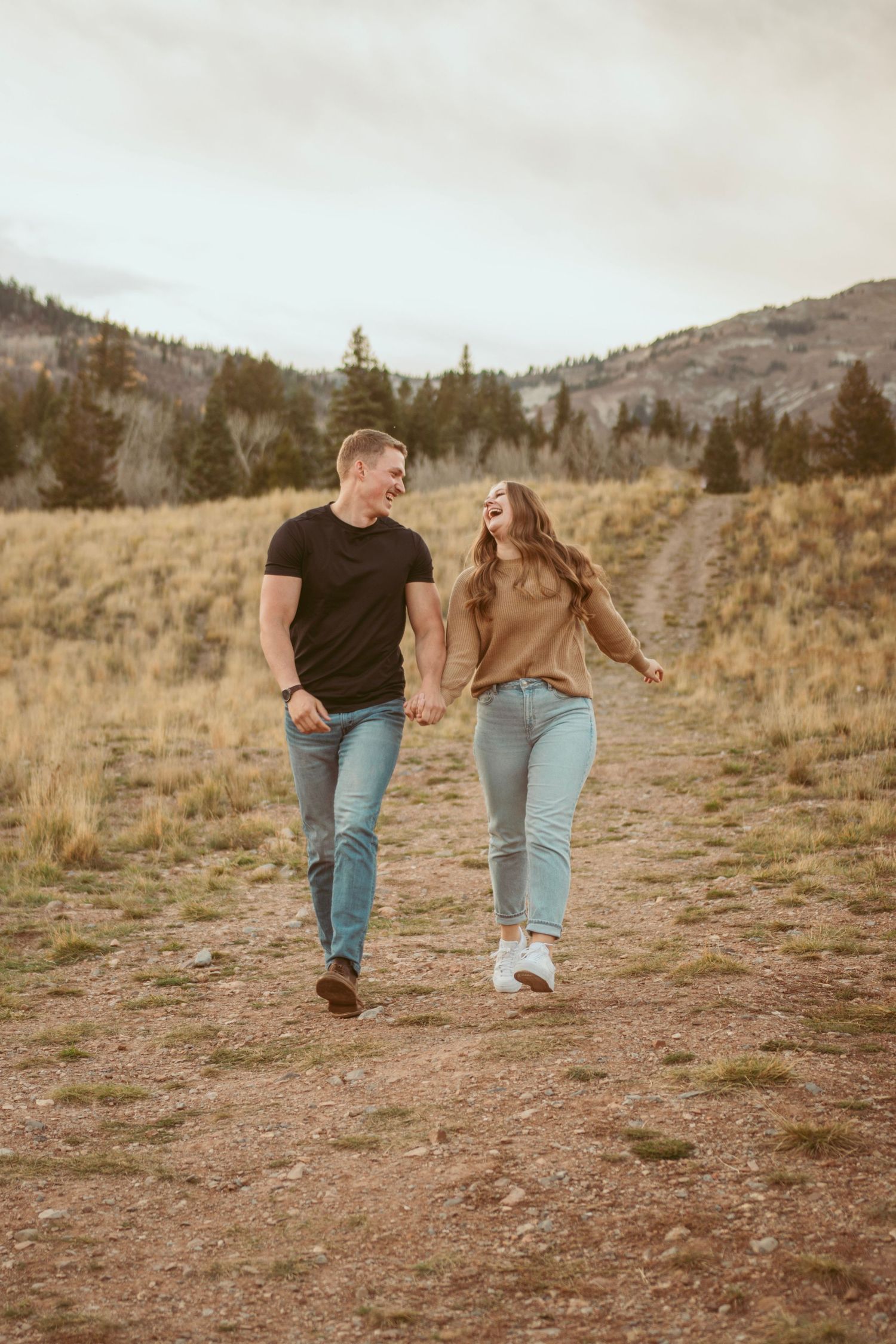 Couple running playfully through mountain meadow at sunset.