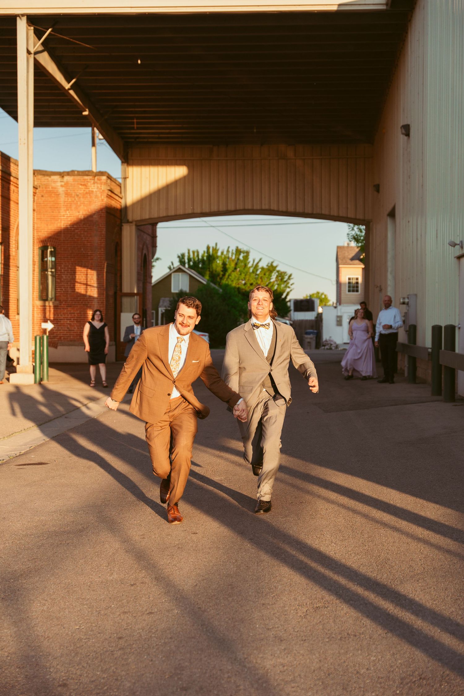 Wedding party members walk together casting long shadows during golden hour at an outdoor venue.