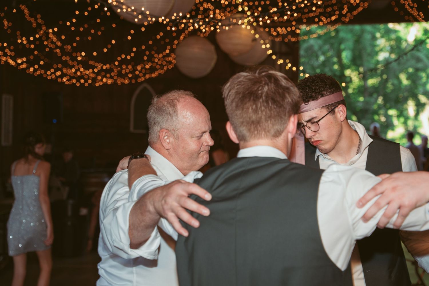 Wedding reception dance floor filled with guests under string lights and lanterns.