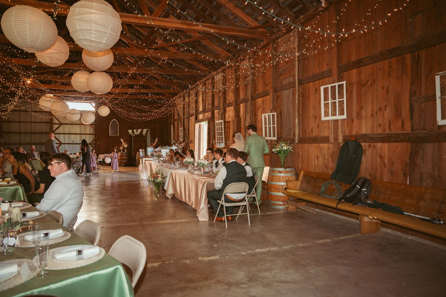 Rustic barn interior decorated with string lights and white paper lanterns for a wedding.