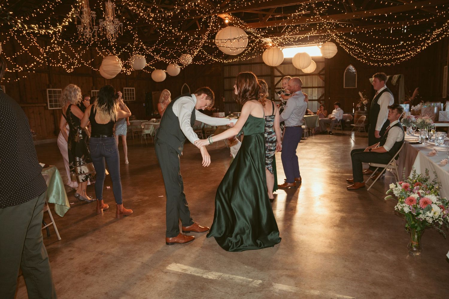 Wedding guests dancing in a dimly lit barn venue decorated with string lights and white lanterns.