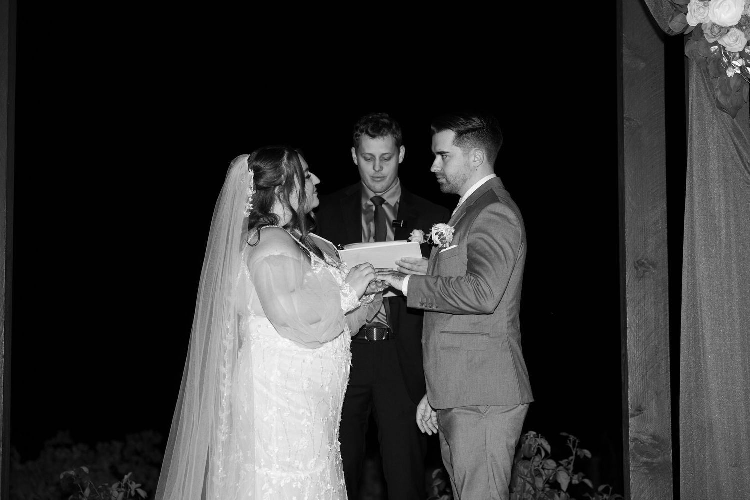 Romantic nighttime wedding ceremony with couple under illuminated gazebo.