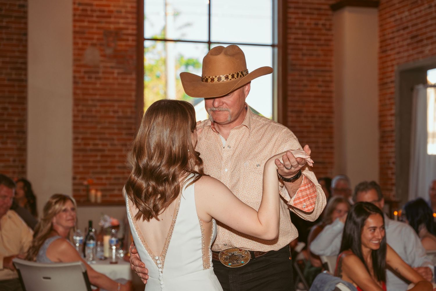 Wedding celebration dance in progress at industrial venue with exposed brick walls.