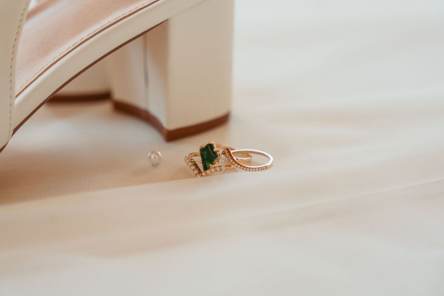 Close-up of an emerald engagement ring with rose gold band against a soft neutral background.