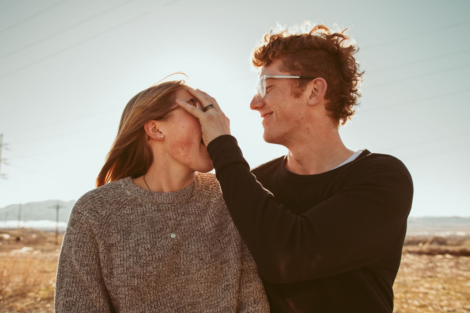 A couple in warm sweaters laughing together against a desert landscape background.