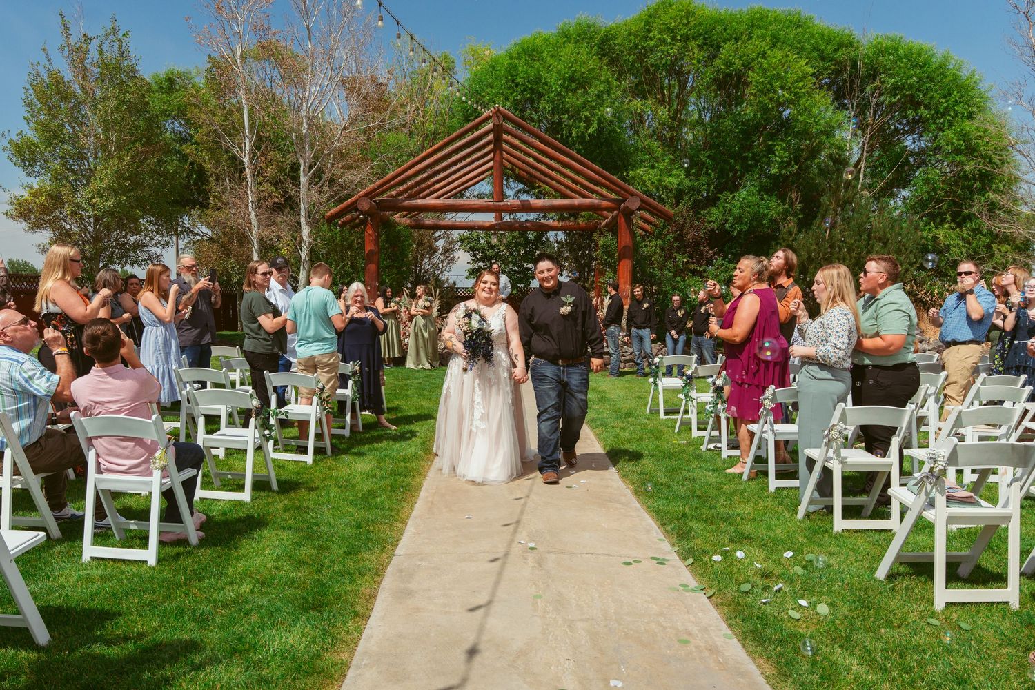 Outdoor wedding ceremony setup with white chairs arranged in rows on a lush green lawn under blue skies.