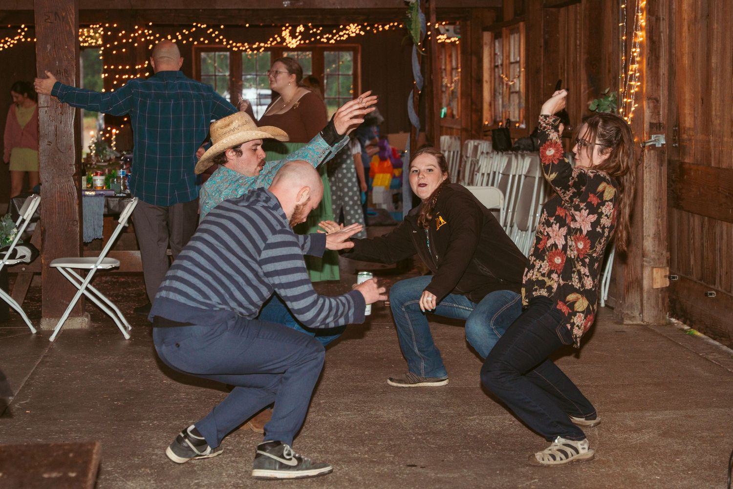 Guests enjoy dancing and socializing at a barn party with string light decorations.