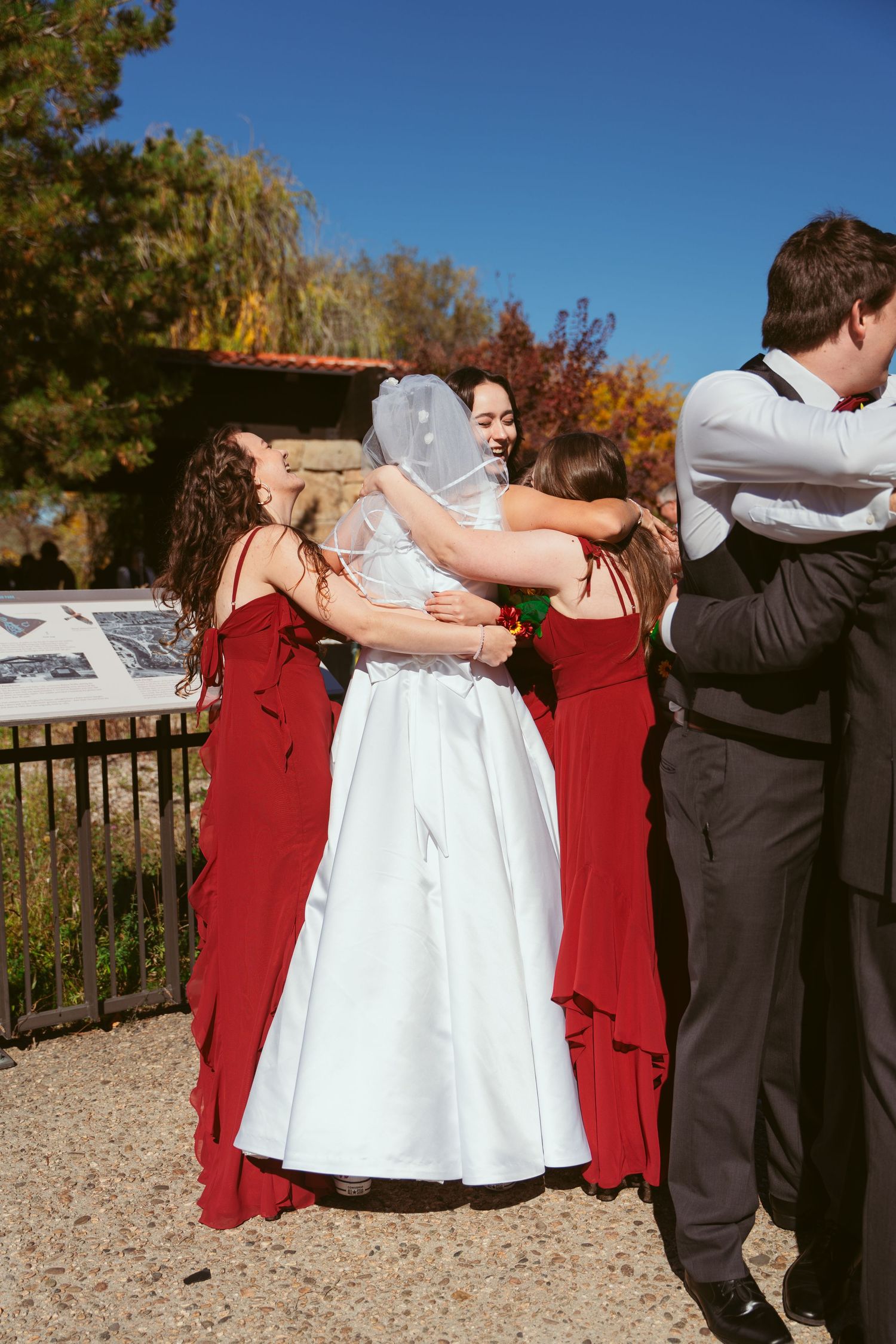 Wedding party in burgundy and formal attire posing together on outdoor path.