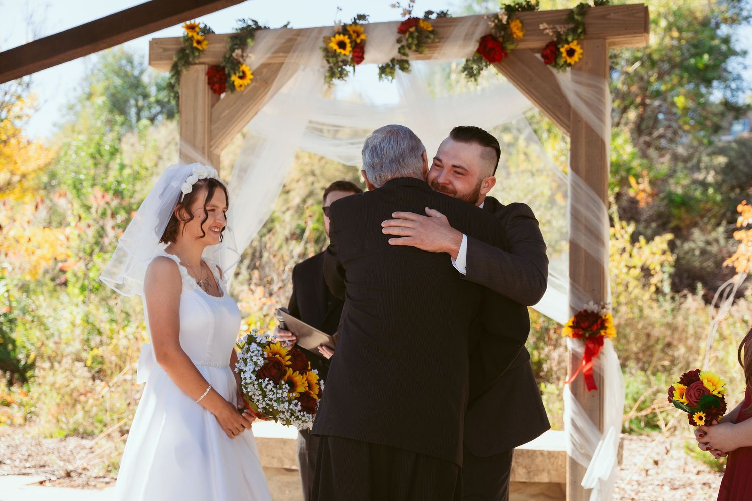 Emotional moment during wedding ceremony under pergola decorated with sunflowers.