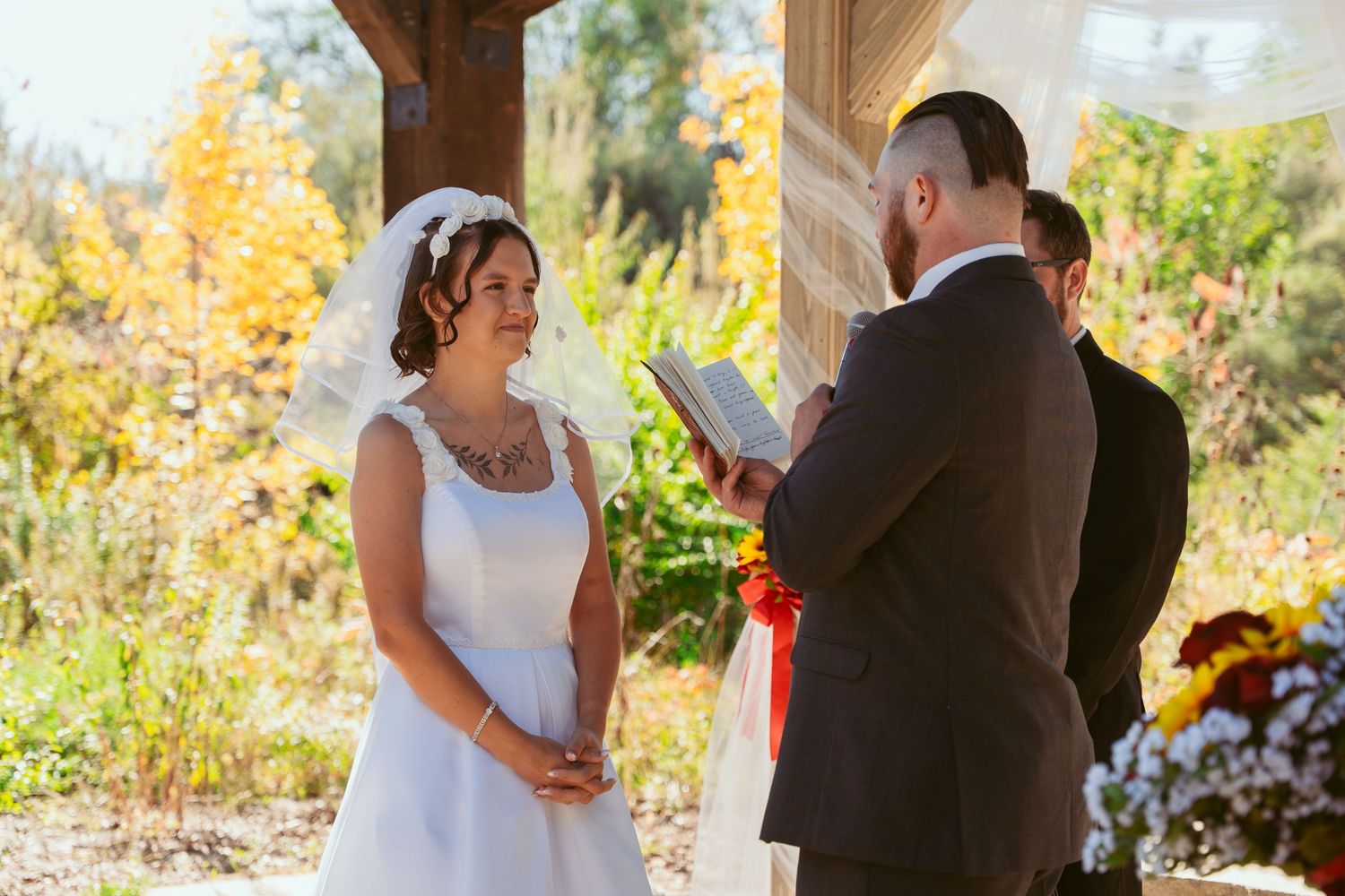 Autumn wedding ceremony under wooden beams with sunflower decorations and natural lighting.