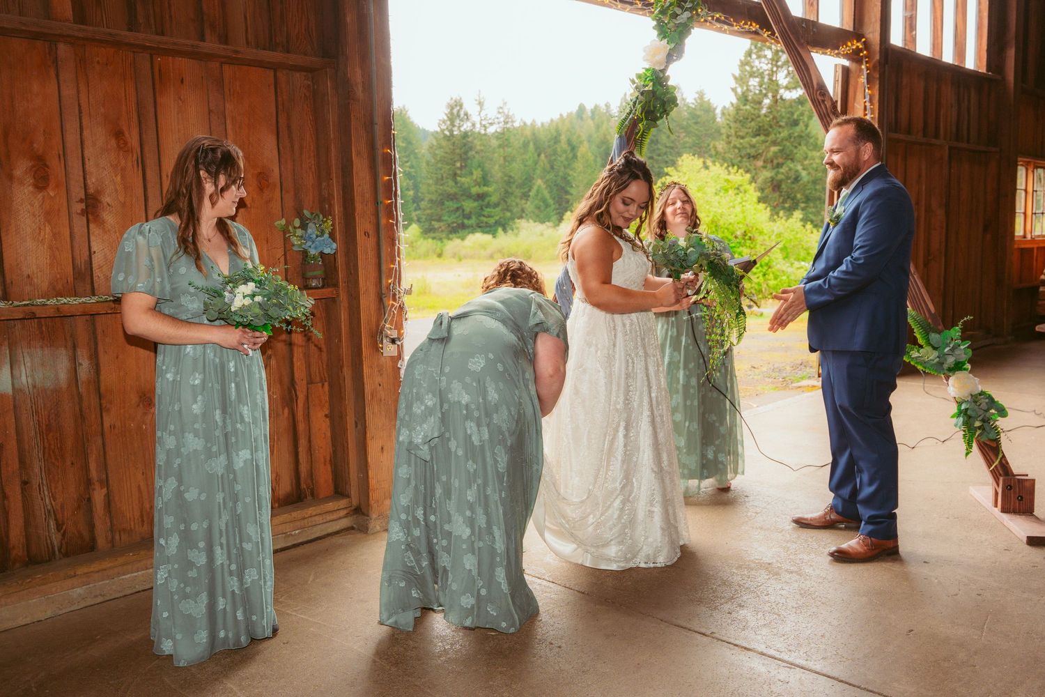 Wedding party posing in rustic barn setting with natural light streaming through windows.
