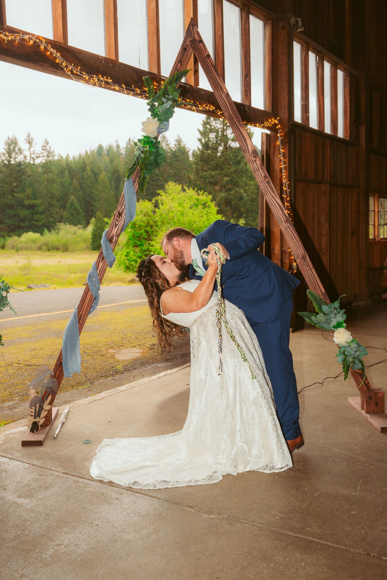 Romantic dance poses inside rustic barn with string lights and wooden beams.