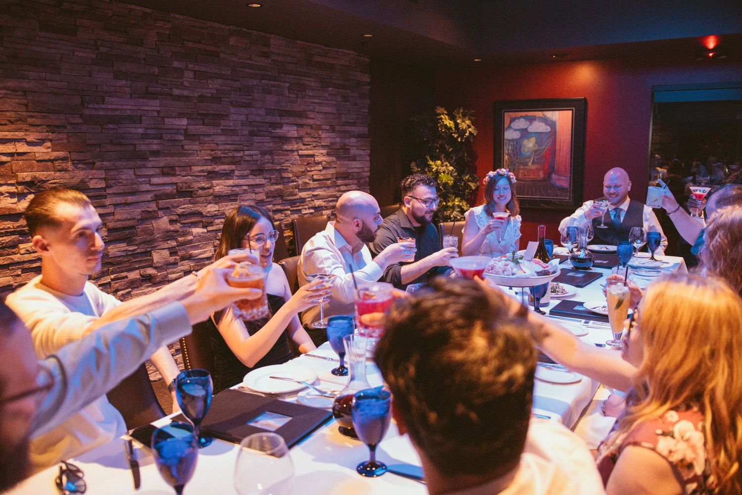 Wedding guests raise glasses for a toast during reception dinner at a restaurant with stone walls.