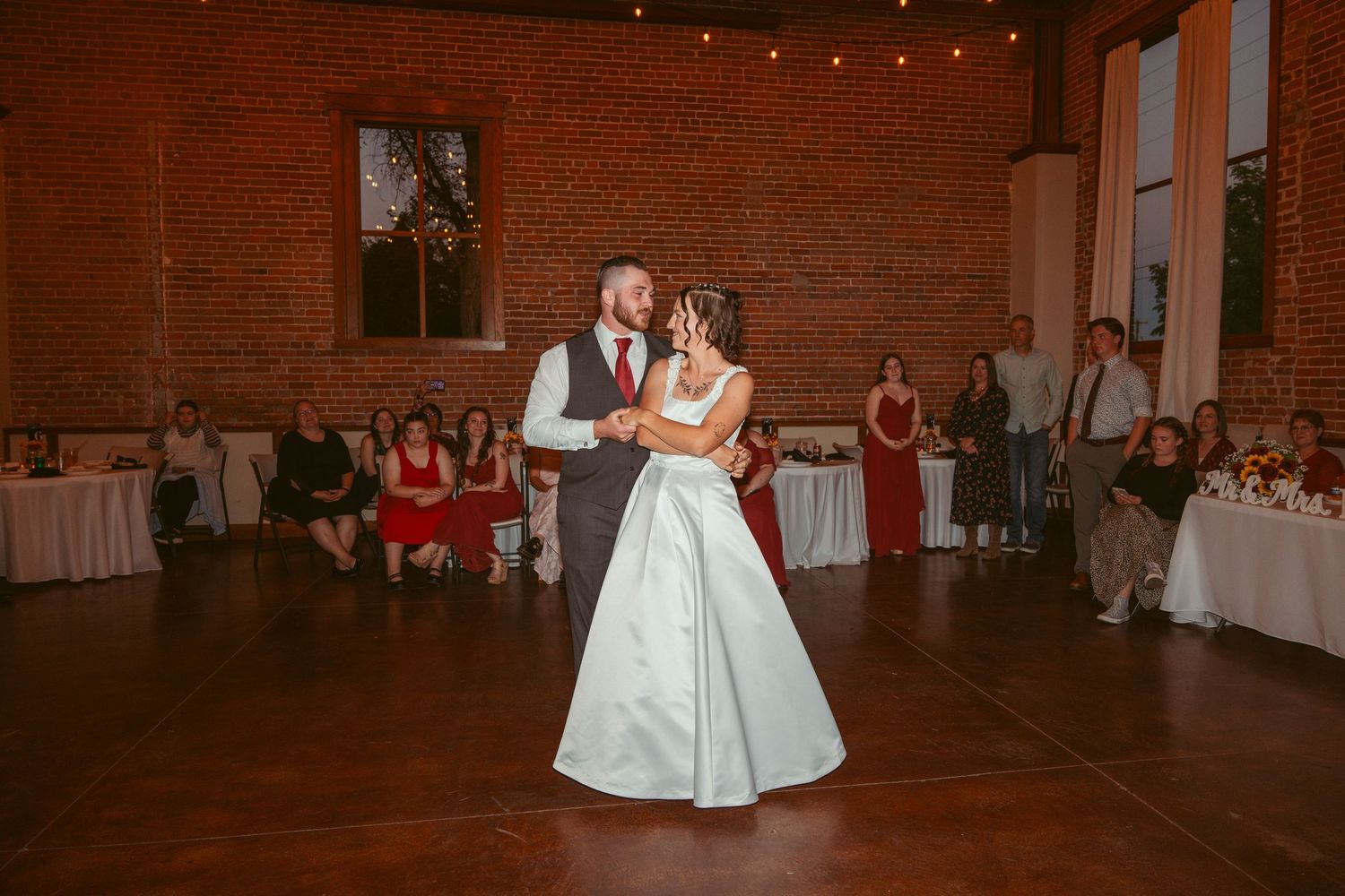 Couple shares an intimate dance in a rustic reception space with exposed brick walls.