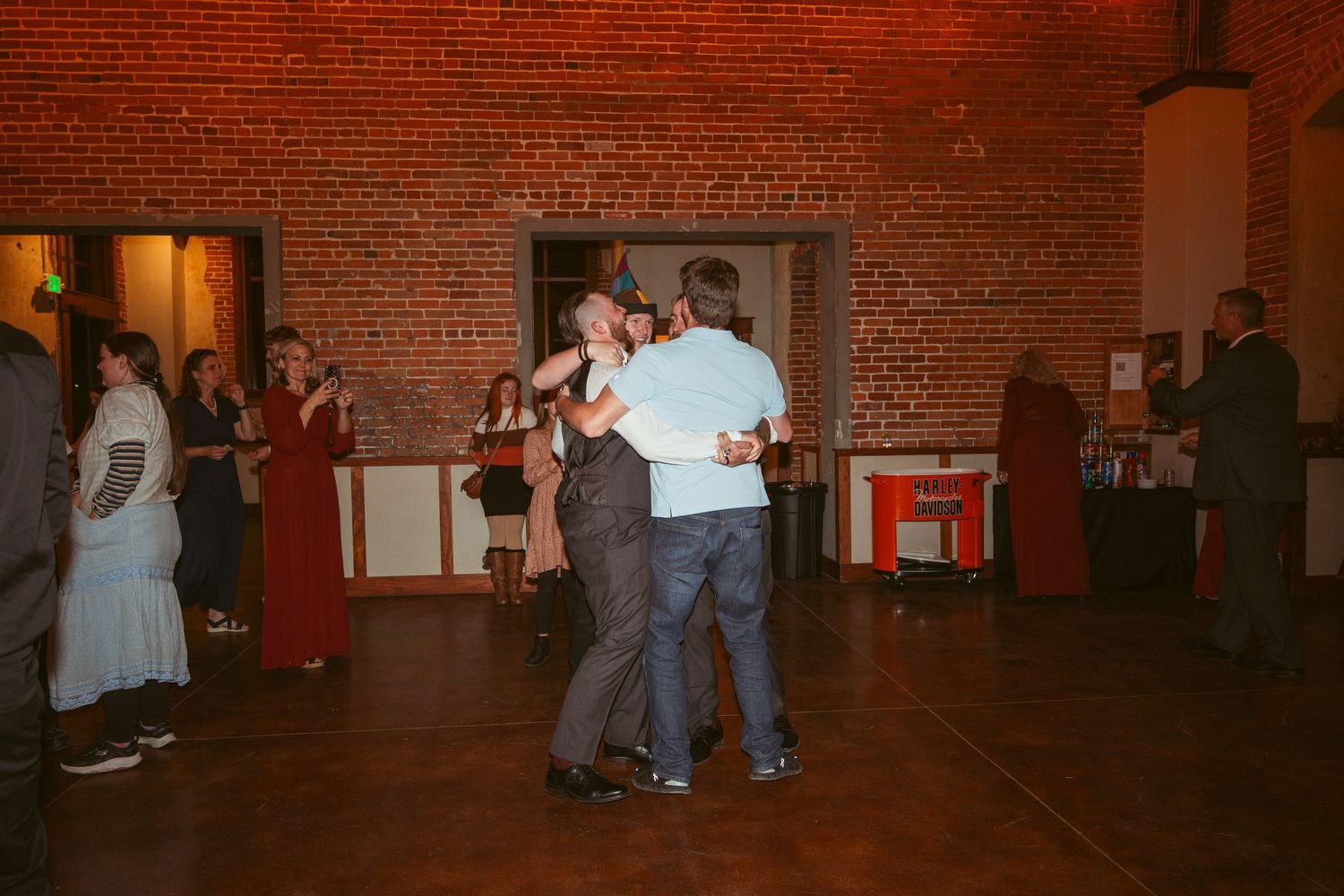Wedding celebration with dancing guests in a dimly lit brick venue.
