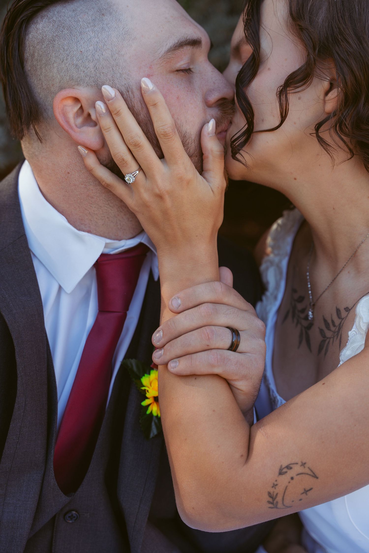 Close-up of tender moment between newlyweds with burgundy tie and floral boutonniere.