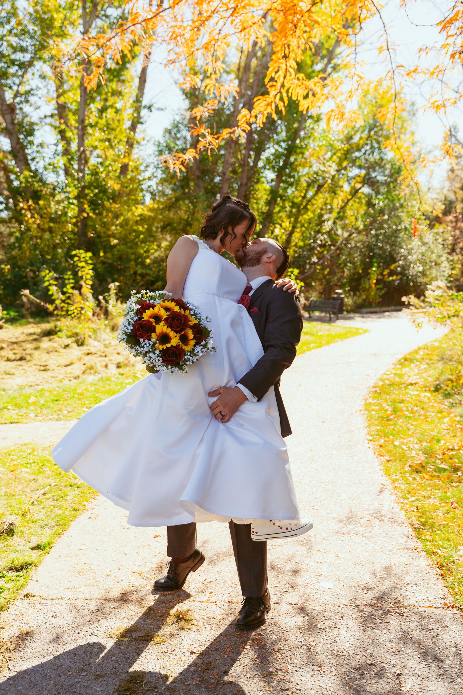 A couple performs a dramatic dance dip on a forest path with autumn colors.