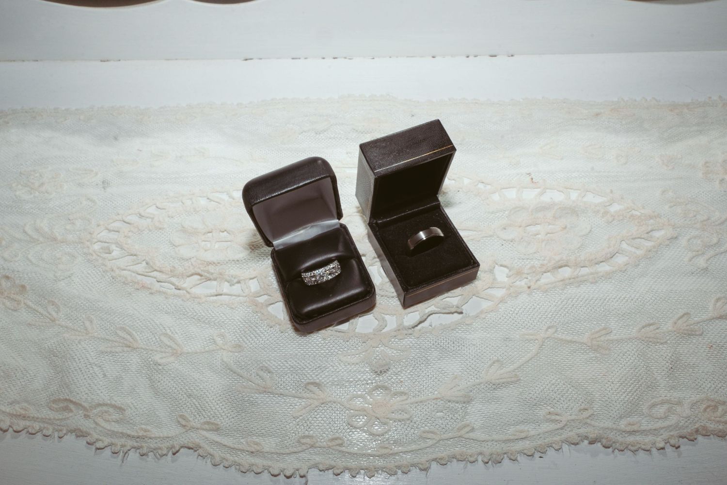 Wedding rings displayed in dark brown wooden boxes on white lace tablecloth.