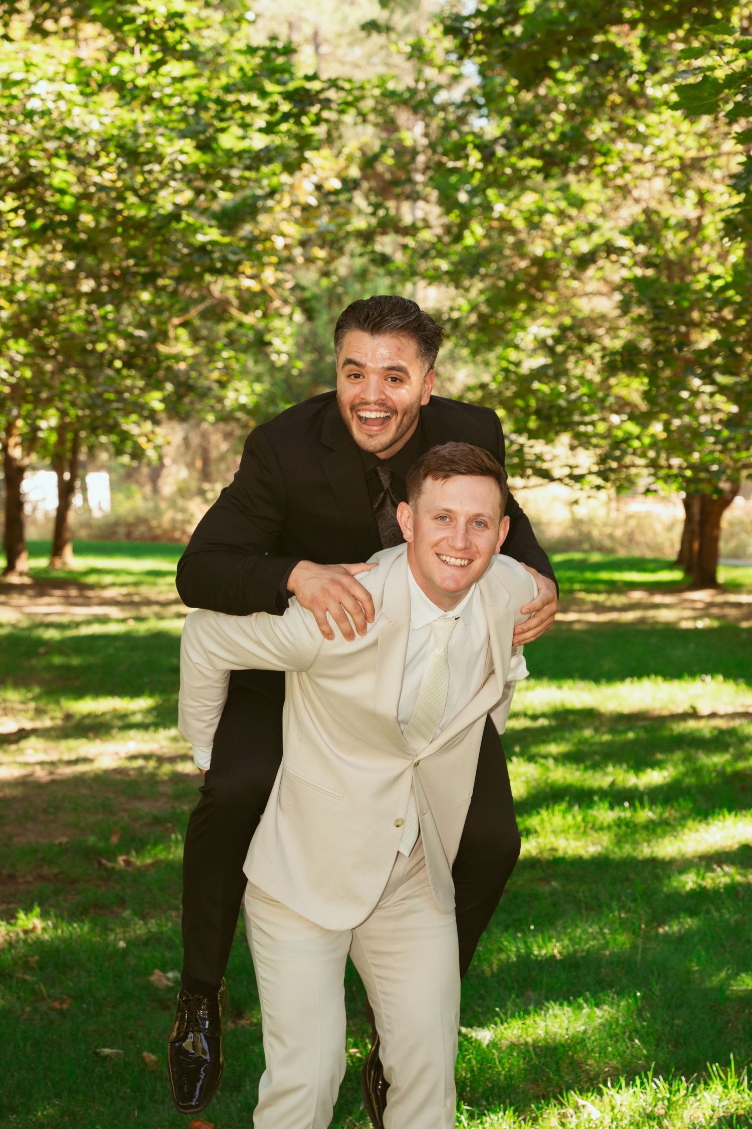 Groomsmen in light and dark suits share playful moments in a park setting.